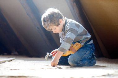 Little kid boy helping with toy tools on construction site. Funny child of 6 years having fun on building new family home. Kid with nails and hammer helping father to renovate old house. clipart