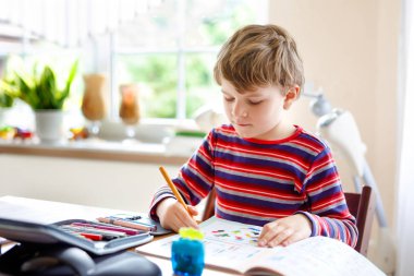 Mutlu gülümseyen küçük çocuk sabah okul başlamadan önce evde ödev yapıyor. Küçük bir çocuk içeride egzersiz yapıyor. İlkokul ve eğitim: Çocuk geometrik figürler çiziyor
