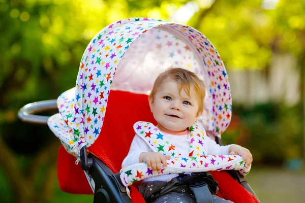 Мила здорова маленька красива дівчинка сидить у колясці або колясці і чекає на маму. Щаслива усміхнена дитина з блакитними очима. З фоном зеленого дерева. Дитяча донька збирається гуляти з сім'єю — стокове фото