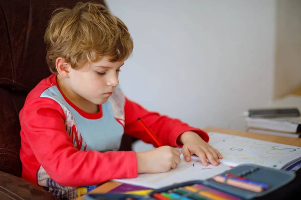 Portrait de mignon garçon heureux d'école à la maison faisant des devoirs. Petit enfant écrivant avec des crayons colorés, à l'intérieur. École primaire et éducation. Enfant apprenant à écrire des lettres et des chiffres — Photo