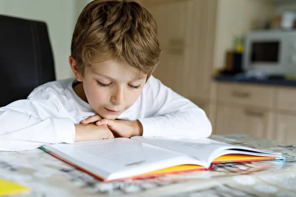 Liten blond skola unge pojke en bok hemma — Stockfoto