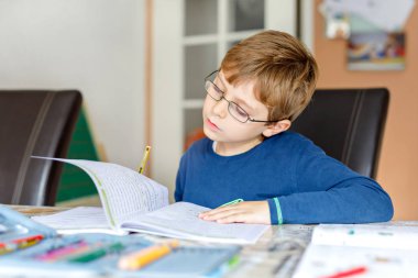 Evde gözlüklü şirin okullu çocuk çocuk portresi ödev yapma. Küçük çocuk renkli kalemler ile kapalı yazma yoğunlaşmıştır. İlköğretim Okulu ve eğitim