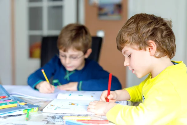 Dois miúdos em casa a fazer trabalhos de casa. Pequenas crianças concentradas escrevendo com lápis coloridos, dentro de casa. Escola primária e educação. Irmãos e melhores amigos aprendendo . — Fotografia de Stock