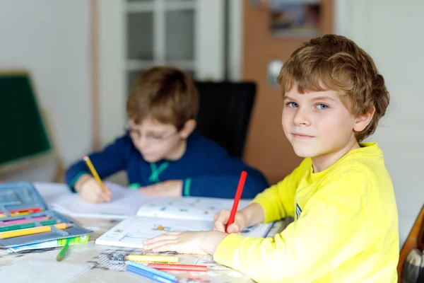 Dois miúdos em casa a fazer trabalhos de casa. Pequenas crianças concentradas escrevendo com lápis coloridos, dentro de casa. Escola primária e educação. Irmãos e melhores amigos aprendendo . — Fotografia de Stock