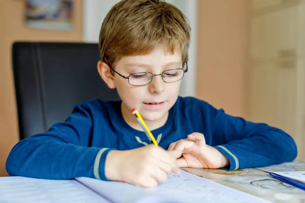 Ritratto di ragazzo carino della scuola con gli occhiali a casa a fare i compiti. Piccolo bambino concentrato che scrive con matite colorate, al chiuso. Scuola elementare e istruzione — Foto Stock