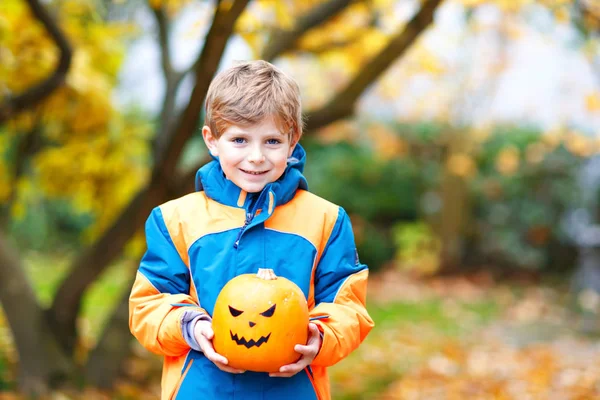 Feliz niño lindo con linterna de calabaza de Halloween. Divertido niño en ropa colorida divirtiéndose y jugando en el jardín de otoño en el frío día otoñal. Scary jack-o-lantern, celebración de vacaciones. — Foto de Stock