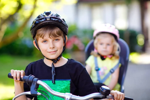 Retrato de menina criança com capacete de segurança sentado no assento da bicicleta do irmão. Rapaz de bicicleta com uma irmã adorável. Conceito de proteção segura e infantil. Família viagem atividade fim de semana . — Fotografia de Stock