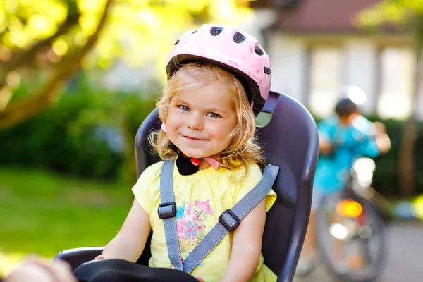 Portret dziewczynki w kasku na głowie, siedzącej na fotelu rodziców. Chłopiec na rowerze w tle. Koncepcja bezpieczeństwa i ochrony dzieci. Wycieczka rodzinna i weekendowa. — Zdjęcie stockowe