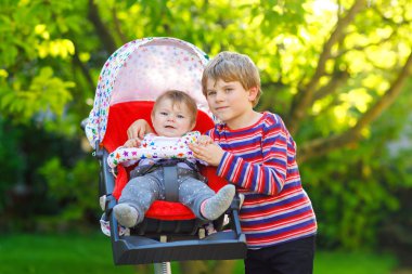 Küçük sarışın çocuk çocuk kardeşim ile oynamak. Mutlu kardeşler Bahçe. Çocuk arabası ya da bebek arabası oturan kız bebek. Kardeşim ve yaz gününde gidiş birlikte bir yürüyüşe şirin toddler açık havada