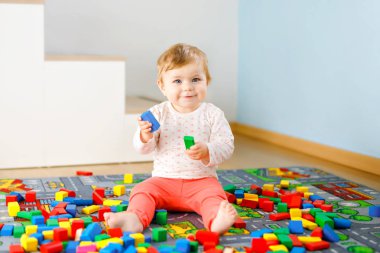 Eğitici oyuncaklarla oynayan sevimli bir kız bebek. Mutlu sağlıklı bir çocuk, evdeki renkli tahta bloklarla eğleniyor. Bebek öğrenme renkleri ve biçimleri