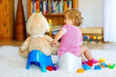 Lazımlık üzerinde oturan sevimli küçük 12 aylık toddler bebek kız çocuk portre. Büyük peluş yumuşak oyuncak ile oynayan çocuk. Tuvalet eğitimi kavramı. Öğrenen, geliştirme adımlar bebek