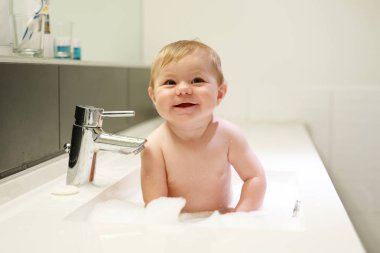 Lavaboda yıkanan, su ve köpükle oynayan sevimli bir bebek.