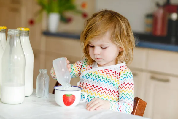 Schattig peutermeisje dat koemelk drinkt als ontbijt. Schattige kleine dochter met veel flessen. Gezond kind dat melk als gezondheidscalciumbron heeft. Kind thuis of in de kinderkamer in de ochtend. — Stockfoto