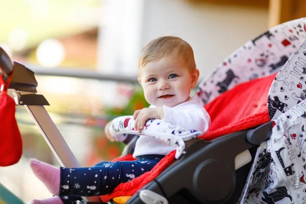 Bonito menina bonita sentada no carrinho de bebê ou carrinho e esperando a mãe. Criança sorridente feliz com olhos azuis . — Fotografia de Stock