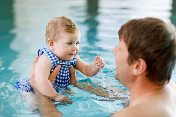 Happy middle-aged father swimming with cute adorable baby girl in swimming pool.