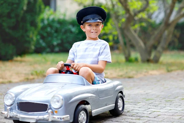 Niño feliz jugando con un gran coche de juguete viejo en el jardín de verano, al aire libre. Un niño sano conduciendo un viejo taxi de coches antiguos. Chico risueño y sonriente. Familia, infancia, concepto de estilo de vida — Foto de Stock