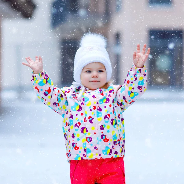 Ritratto di bambina che cammina all'aperto in inverno. Carino il bambino che mangia dolci caramelle lecca lecca. Bambino che si diverte nella fredda giornata sulla neve. Indossare vestiti caldi colorati bambino e cappello con ciambelle. — Foto Stock