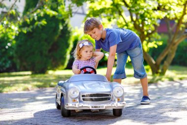 İki mutlu çocuk açık havada, yaz bahçesinde eski oyuncak arabalarıyla oynuyorlar. Küçük bir kızla araba süren bir çocuk, içinde de tatlı bir kız kardeş. Gülen ve gülümseyen çocuklar. Aile, çocukluk, yaşam tarzı konsepti.