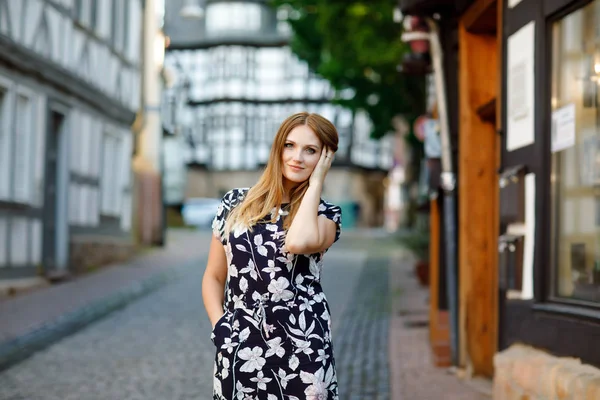 Belle jeune femme aux cheveux longs en robe d'été se promenant dans la ville allemande. Fille heureuse profitant de la marche dans une jolie petite ville fachwerk avec de vieilles maisons en Allemagne. — Photo