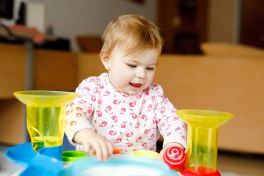 Evde ya da çocuk odasında eğitici oyuncaklarla oynayan sevimli, güzel bir kız bebek. Mutlu sağlıklı çocuk eğleniyor ve farklı renkli plastik topları ayırıyor. Çocuk farklı yetenekler öğreniyor