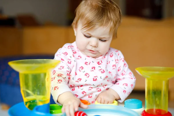 Evde ya da çocuk odasında eğitici oyuncaklarla oynayan sevimli, güzel bir kız bebek. Mutlu sağlıklı çocuk eğleniyor ve farklı renkli plastik topları ayırıyor. Çocuk farklı yetenekler öğreniyor — Stok fotoğraf