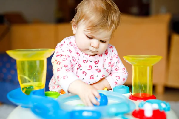 Адекватная симпатичная маленькая девочка, играющая с развивающими игрушками дома или в детском саду. Счастливый здоровый ребенок весело и разноцветными пластиковыми шариками. Ребенок учится различным навыкам — стоковое фото