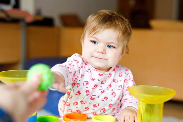 Evde ya da çocuk odasında eğitici oyuncaklarla oynayan sevimli, güzel bir kız bebek. Mutlu sağlıklı çocuk eğleniyor ve farklı renkli plastik topları ayırıyor. Çocuk farklı yetenekler öğreniyor — Stok fotoğraf