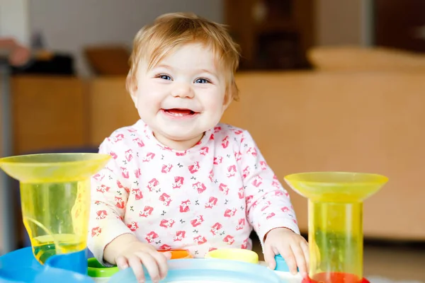 Evde ya da çocuk odasında eğitici oyuncaklarla oynayan sevimli, güzel bir kız bebek. Mutlu sağlıklı çocuk eğleniyor ve farklı renkli plastik topları ayırıyor. Çocuk farklı yetenekler öğreniyor — Stok fotoğraf