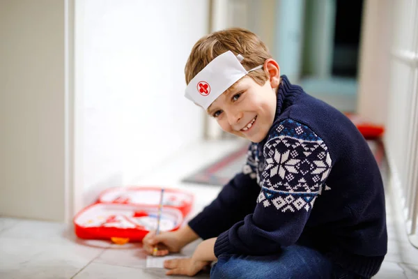 Roztomilá malá školní chlapečka, co hraje na doktora s hračkou. Šťastné zdravé dítě, které se baví s rolí a přemýšlí o budoucí práci v nemocnici — Stock fotografie