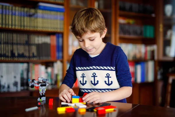 金发小子玩了很多五颜六色的塑料块。可爱的学校男孩与建设和创造机器人的乐趣。创意休闲现代科技与机器人. — 图库照片