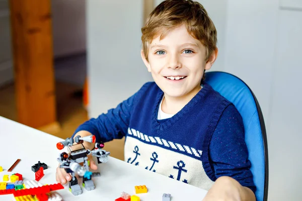 Criança loira brincando com muitos blocos de plástico coloridos. Menino da escola bonito se divertindo com a construção e criação de robô. Lazer criativo moderno técnico e robótico . — Fotografia de Stock