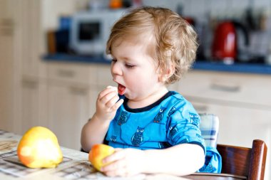 Tatlı, tapılası bir kız taze armut yiyor. Bir yıllık aç, mutlu bir bebek elinde meyve tutuyor..