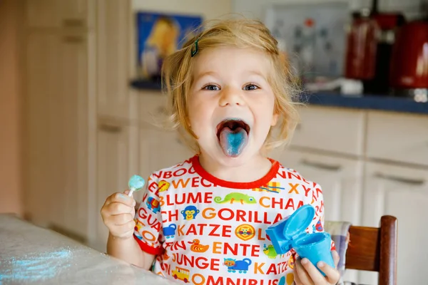 Gorgeous Little maluch lizanie lizaki dziewczyna i pokazując kolorowy niebieski język. Zabawne dziecko bawiące się z kolorowania Bonbon, wewnątrz — Zdjęcie stockowe