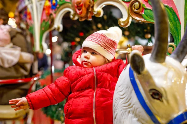 Entzückendes kleines Mädchen, das auf einem Karussell auf dem Weihnachtsmarkt oder Markt im Freien reitet. fröhliches Kleinkind hat Spaß auf traditionellem Familien-Weihnachtsmarkt in Deutschland — Stockfoto