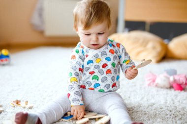 Evde ya da çocuk odasında ahşap yapboz gibi eğitici oyuncaklarla oynayan güzel bir kız bebek. Mutlu sağlıklı çocuk renkli oyuncaklarla eğleniyor. Çocuk farklı yetenekler öğreniyor