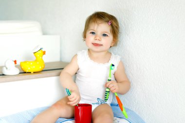 Küçük kız diş fırçası tutuyor ve ilk dişlerini fırçalıyor. Bebek süt dişini temizlemeyi öğreniyor..