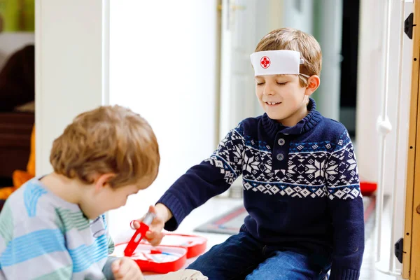 Dos niños de la escuela jugando al doctor con un juego de juguetes. Niños sanos felices, hermanos y mejores amigos divirtiéndose con juegos de rol y pensando en el futuro trabajo en el hospital — Foto de Stock