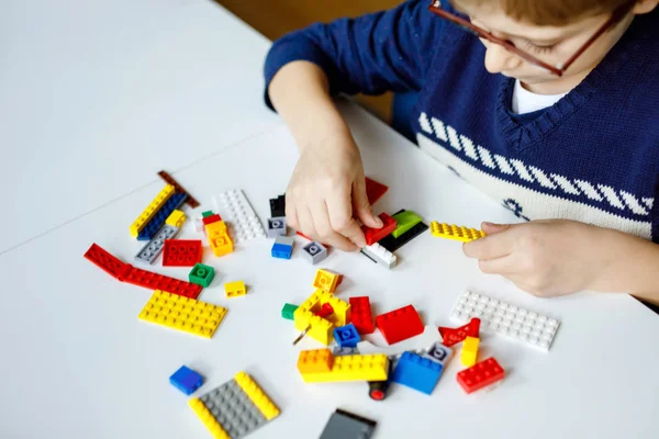 Petit enfant blond avec des lunettes jouant avec beaucoup de blocs en plastique coloré. Adorable écolier qui s'amuse avec la construction et la création de robots. Loisirs créatifs technique moderne et robotique. — Photo