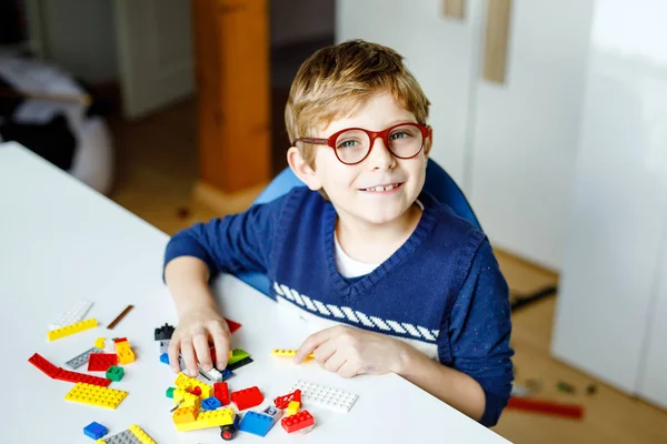 Petit enfant blond avec des lunettes jouant avec beaucoup de blocs en plastique coloré. Adorable écolier qui s'amuse avec la construction et la création de robots. Loisirs créatifs technique moderne et robotique. — Photo