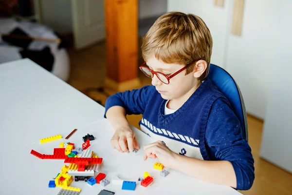 Petit enfant blond avec des lunettes jouant avec beaucoup de blocs en plastique coloré. Adorable écolier qui s'amuse avec la construction et la création de robots. Loisirs créatifs technique moderne et robotique. — Photo