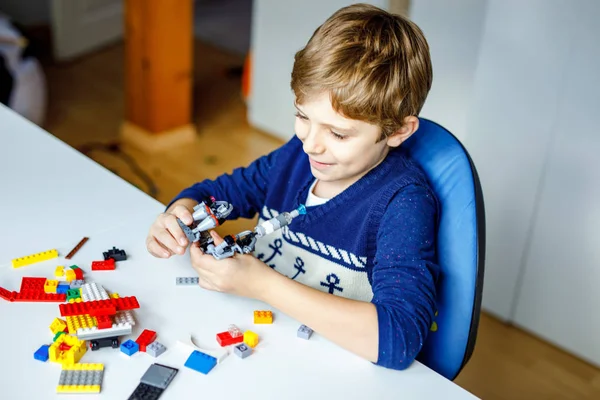 Criança loira brincando com muitos blocos de plástico coloridos. Menino da escola bonito se divertindo com a construção e criação de robô. Lazer criativo moderno técnico e robótico . — Fotografia de Stock