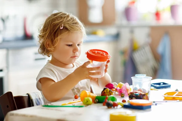 Adorable linda niña pequeña con arcilla colorida. Bebé saludable jugando y creando juguetes a partir de masa de juego. Moldeo de niños pequeños modelado de arcilla y aprendizaje — Foto de Stock