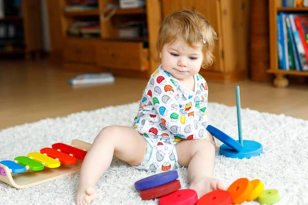 Адекватная симпатичная маленькая девочка, играющая с учебными деревянными игрушками дома или в детском саду. Тоддлер с красочной пирамидой стека — стоковое фото