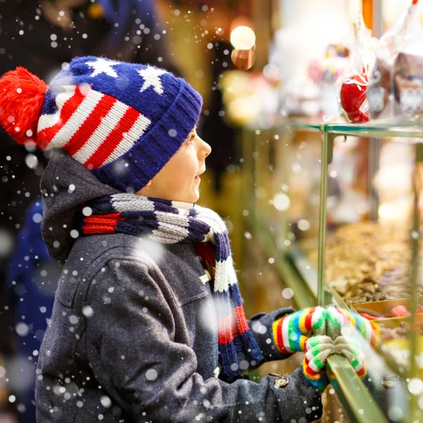 Roztomilé dítě chlapeček poblíž sweet stojan s ořechy a perníčky. Šťastné dítě na vánoční trh v Německu. Tradiční volný pro rodiny na Vánoce. Dovolená, oslavy, tradice, dětství. — Stock fotografie