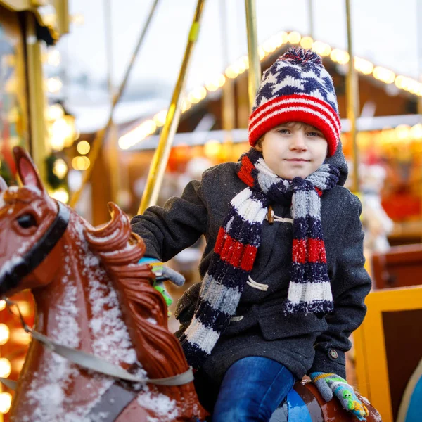 Adorable niño montado en un alegre paseo en carrusel caballo en la feria de Navidad o mercado, al aire libre. Feliz niño divirtiéndose en el tradicional mercado de Navidad familiar en Hamburgo, Alemania . — Foto de Stock