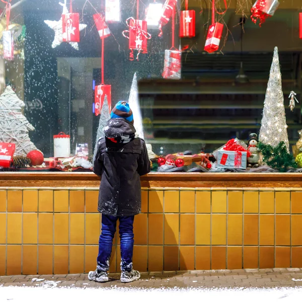 Cute little school kid boy on Christmas market. Funny happy child in fashion winter clothes making window shopping decorated with gifts, xmas tree. holidays, christmas, childhood and people concept. — Stock Photo, Image