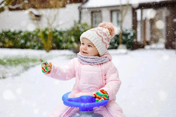 Schattig klein peuter meisje geniet van een slee rit op sneeuw. Kindersleeën. Baby kind rijden een slee in kleurrijke mode kleding. Buiten actief plezier voor familie wintervakantie op dag met sneeuw — Stockfoto
