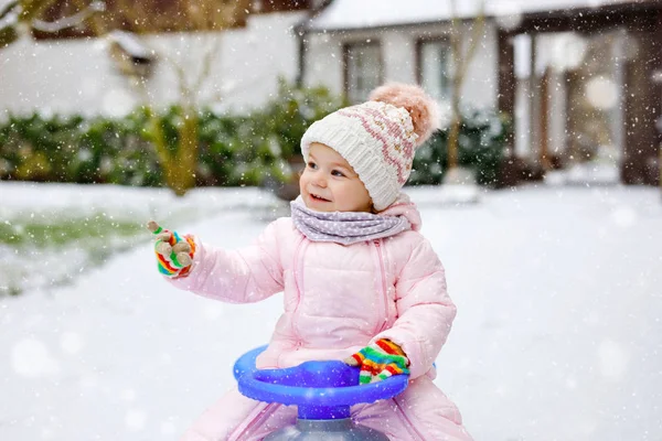 Söt liten småbarn flicka njuter av en släde rida på snö. Barnspann. Baby kid rider en släde i färgglada mode kläder. Utomhus aktivt roligt för familjen vintersemester på dagen med snöfall — Stockfoto