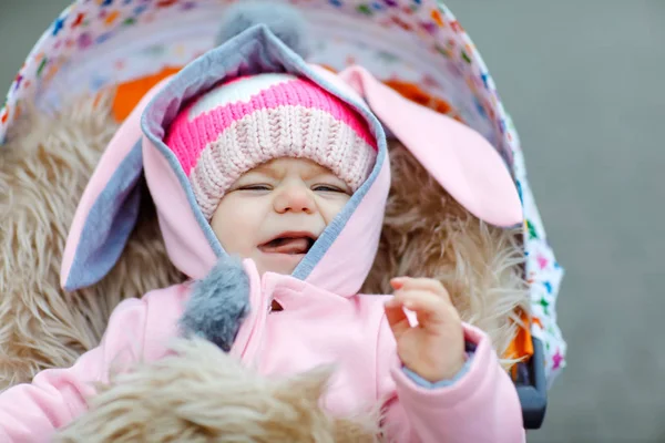 Cute little beautiful baby girl sitting in the pram or stroller on autumn day. Happy smiling child in warm clothes, fashion stylish baby coat. Healthy toddler going for walk on fresh air with parents — Stock Photo, Image