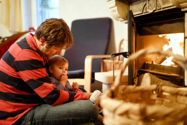 Middle age father sitting by fireplace with cute little baby girl at home. Happy family, dad with daughter make fire for Christmas time. Safe handling for kids